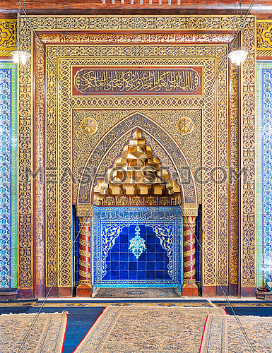 Golden ornate arched mihrab (niche) with floral pattern, blue Turkish ceramic tiles and arabic calligraphy at the public mosque of The Manial Palace of Prince Mohammed Ali Tewfik, Cairo, Egypt