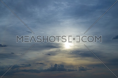 Glowing sun peeking through the clouds at sunset in a twilight blue sky in a nature or weather background with copy space