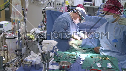 Pan right long shot of operating room while medical team performing surgery