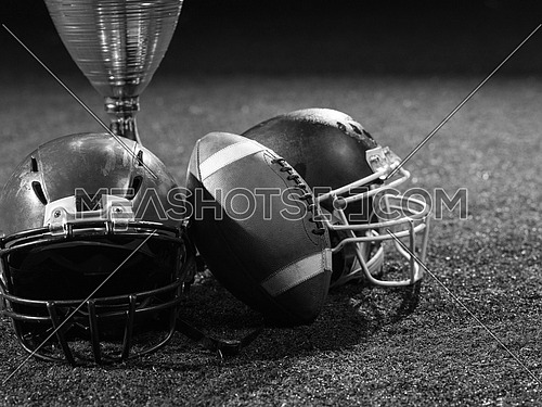 closeup shot of american football,helmets and trophy on grass field at night