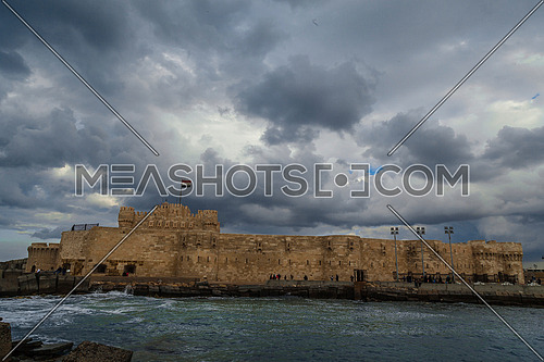 Long Shot outside Citadel of Qaitbay shows sea waves at Cloudy day to night