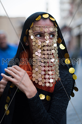 portrait of a young middle eastern woman in a traditional costume with gold coins over her face