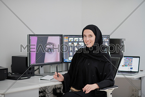 Portrait of young muslim female graphic designer. Hijab girl with the two monitors in background showing her work. Technology concept