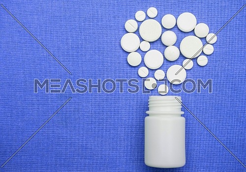 Pills coming out white pot forming an isolated heart in green background, conceptual image