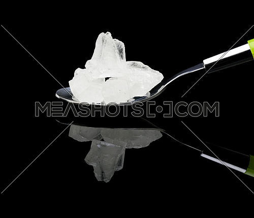 crystal sugar on a spoon over black reflective surface background