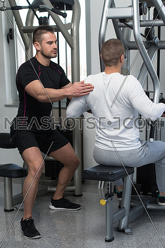 Personal Trainer Showing Young Man How To Train Back On Machine In The Gym