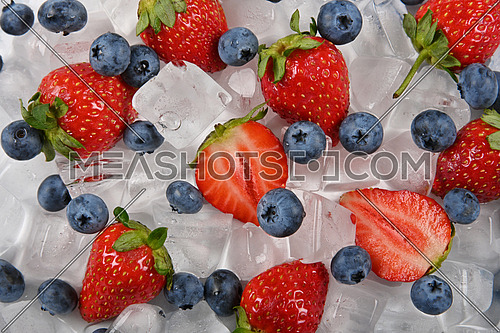 Close up fresh red ripe strawberries, blueberries and ice cubes on table, elevated high angle view, directly above