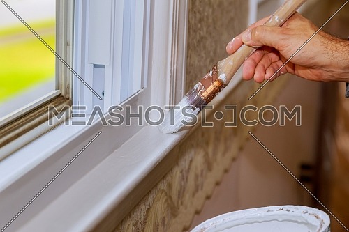 Closeup image of mans hand with paintbrush while painting window trim