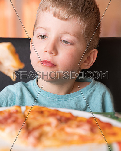 Kid boy eats pizza sitting at the table