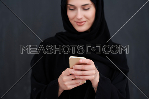 Young muslim businesswoman in traditional clothes or abaya using smartphone. Arab woman standing in front of black chalkboard and representing techology, islamic  fashion and Ramadan kareem concept
