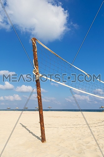 Torn volleyball net on the beach with cloudy blue sky and yellow sand in the morning