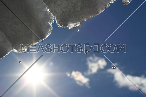 Snow and ice melting and dripping from a roof against the sun and blue skies
