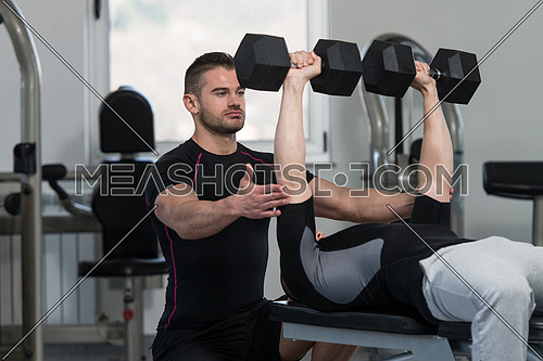 Personal Trainer Showing Young Man How To Train Chest Exercise With Dumbbells In A Health And Fitness Concept