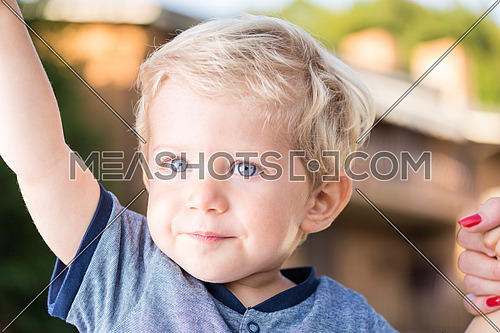 Beautiful baby boy with blue eyes and blond hair holding hands, natural light close up photo