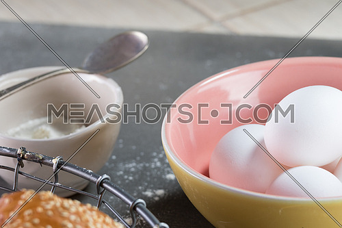 Eggs in a pink yellow bowl aside beige bowl with flour in it