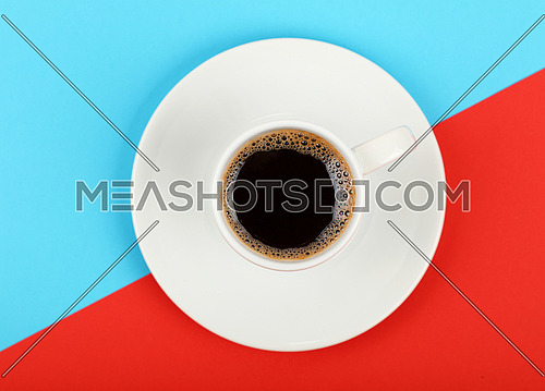 Close up one white cup full of black coffee on saucer over colorful red and blue background, elevated top view, directly above