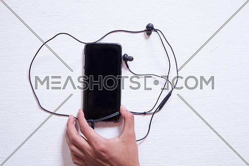 A mobile phone with headphones on a white table
