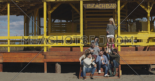 Happy Group Of Friends Hanging Out At Beach House having fun and drinking beer on autumn day