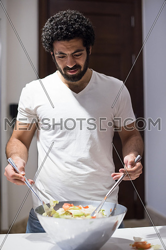 young middle east  man preparing salad in the kitchen with satisfaction