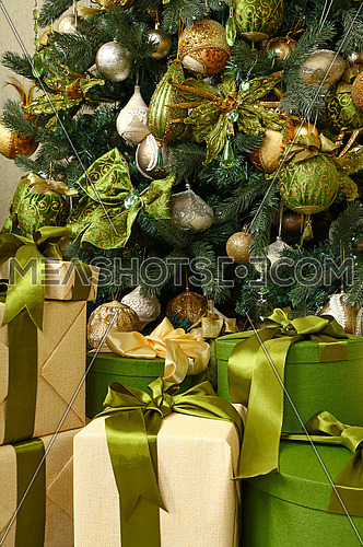Close up green and beige paper wrapped gift boxes with ribbon bows under decorated Christmas tree, high angle front view