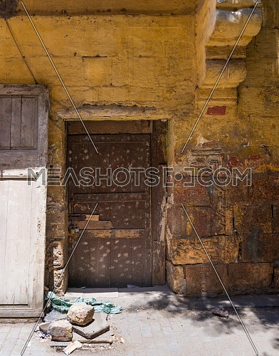 Broken wooden brown door on grunge stone bricks wall painted in orange in abandoned Darb El Labana district, Cairo, Egypt