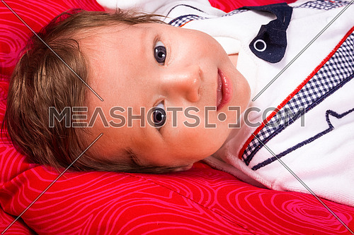 Image of cute newborn boy smiling, closeup portrait of adorable child  on red background.