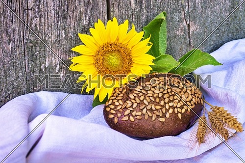 Healthy loaf of brown wholewheat bread coated in sunflower seeds with colorful fresh yellow sunflower and golden ears of wheat in a food still life