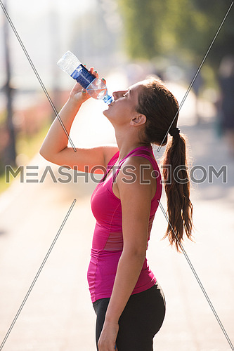 Athlete woman drinking water from a bottle after jogging in the city on a sunny day