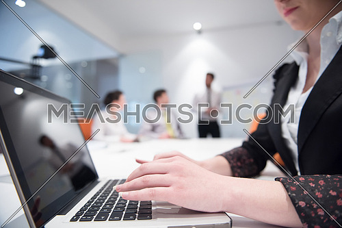business woman hands typing on laptop  computer  on meeting, blurred people group brainstorming in background  at modern bright office interior