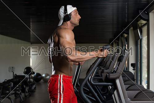 Muscular Mature Man Doing Aerobics Elliptical Walker In Modern Fitness Center