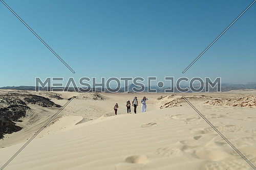 Group of tourists walking on sands with bedouin guide while exploring Sinai Trail from Ain Hodouda at day.