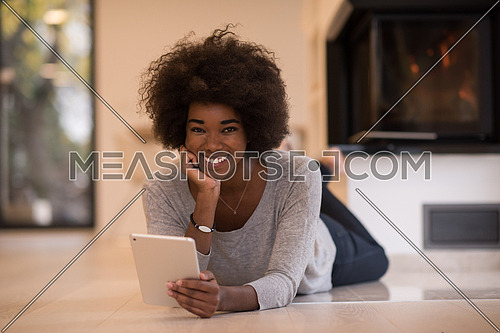 beautiful young black women used tablet computer on the floor of her luxury home in front of fireplace autumn day