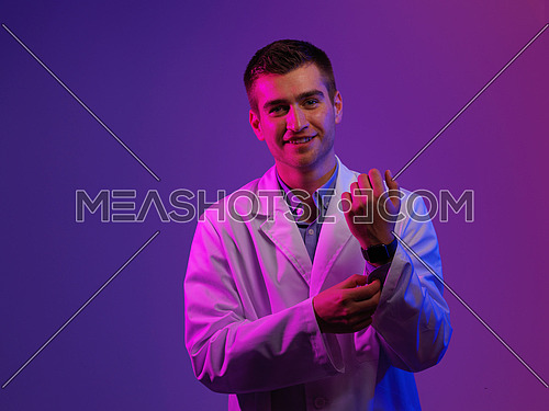 Portrait of hero in white coat.  Cheerful smiling young doctor with stethoscope in medical hospital standing against blue and pink background. Coronavirus covid-19 danger alert