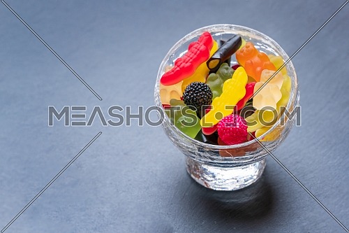 Colored candies inside a glass cup on dark background. Top view with space for your greetings