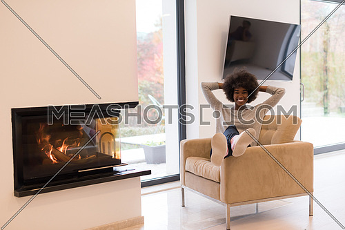 Young beautiful african american woman relaxing on chair in front of fireplace at autumn day