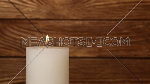 Close up one white candle trembling flame over background of old brown wooden planks wall, off-center, fired up with lighter, burning and blown out