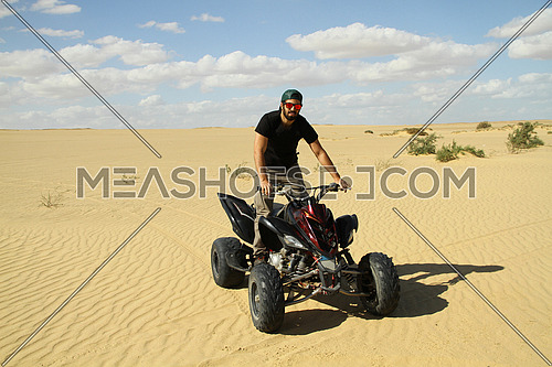 young middle eastern quad motorcycle driver enjoys driving around the desert on a sunny day