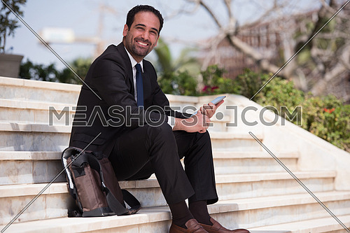 Business executive sitting on the steps of a corporate building working with his tablet