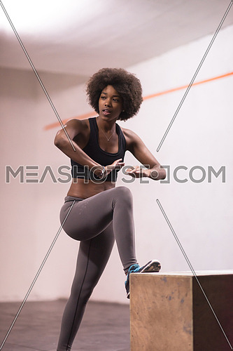Fit young african american woman are preparing for box jumping at a crossfit style gym. Female athlete is performing box jumps at gym.