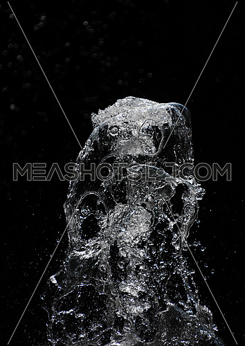 Fountain transparent water stream, splash and drops in motion over black background