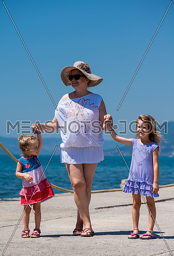 Portrait of a grandmother with her cute little granddaughters holding their hands while standing on the beach coast during Summer vacation