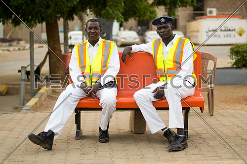 two sudanese traffic police men sitting on a bench posing to the camera
