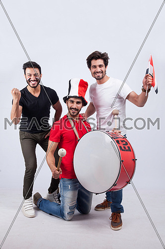 Three young men standing on a white background cheering with a drum for Egypt