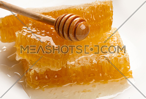 Close up stack of several fresh cut golden comb honey slices and natural wooden dipper on plate isolated on white background, high angle view