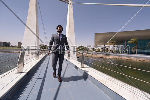 young middle eastern  businessman walking across modern bridge