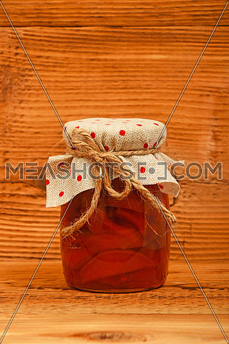 One glass jar of homemade quince jam with textile top decoration at unpainted brown vintage wood