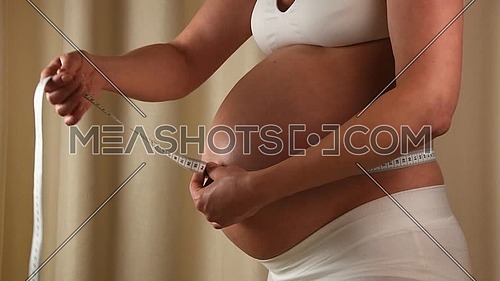 Close up profile view of pregnant Caucasian woman checking her exposed belly with tape measure, slow motion