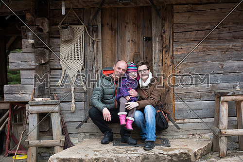 portrait of young family with little child sitting together in front of old retro wooden house