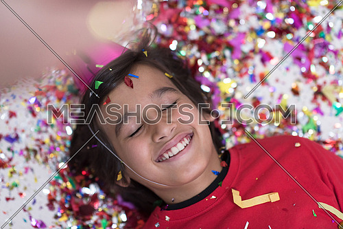 Happy kid celebrating party with blowing confetti while lying on the floor