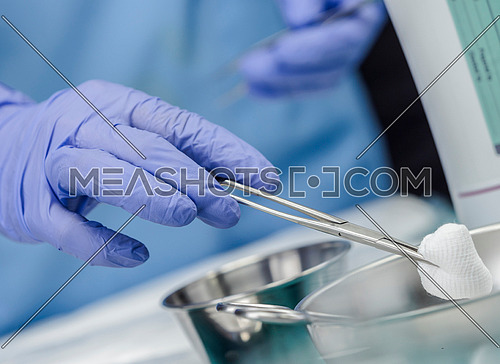 Surgeon working in operating room, hands with gloves holding scissors with torunda, conceptual image, horizontal composition